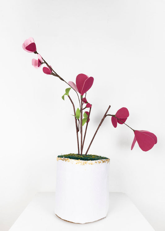 A handmade artificial plant with pink paper petals in a white, textured pot with gold flecked trim