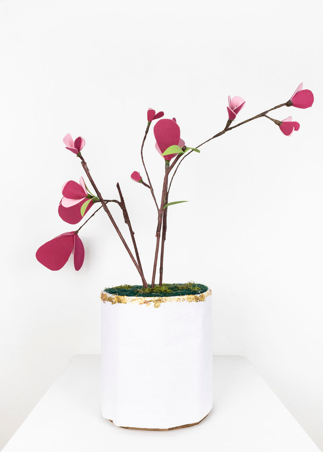 A handmade artificial plant with pink paper petals in a white, textured pot with gold flecked trim