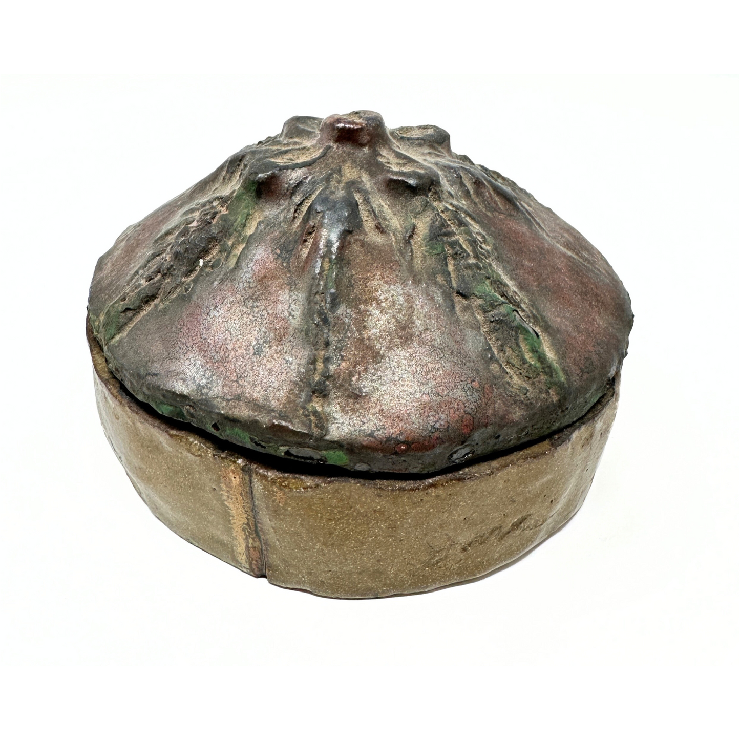 a ceramic container with a circular base and a domed lid. The lid has floral designs sculpted on it, with a flower at the center and vines radiating out and down the sides. The base is glazed brown and the lid is glazed brown and green. 