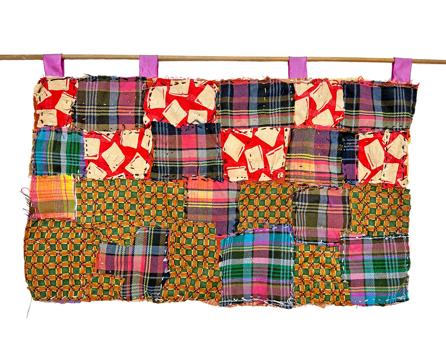 A long rectangular quilt made up of different square fabric swatches, hanging on a wooden dowel from 4 purple fabric loops. The patterns of the fabric swatches are purple plaid, checkered green and orange fabric, and a red fabric with white square designs. The quilt is hand sewn with a running stitch in yellow and purple thread. 