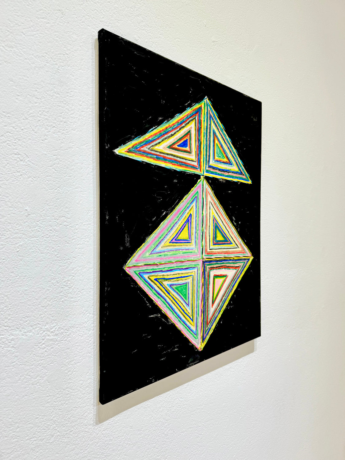 Side view of a painting featuring colorful geometric triangle design on a black background.