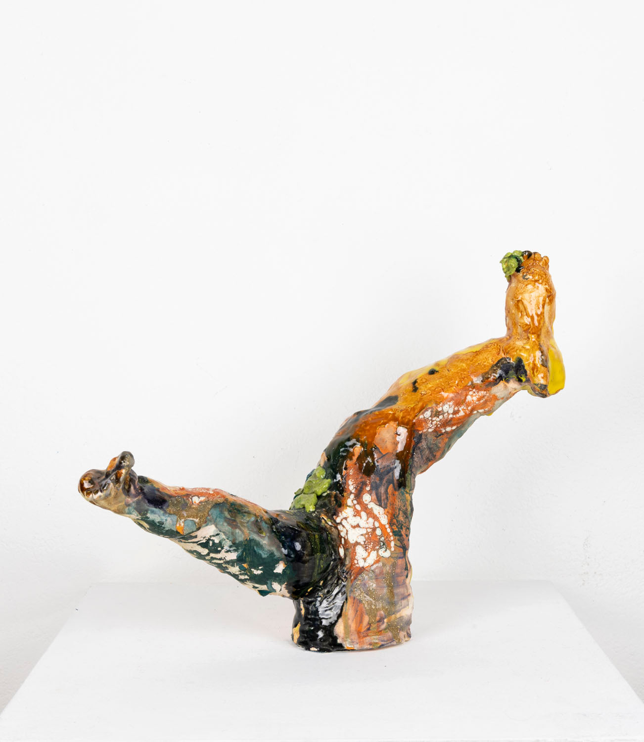 This is an abstract ceramic sculpture that resembles two upward-extending legs. The glossy surface features layered glazes, underglazes and Egyptian paste in earthy tones—rust orange, deep green, black, cream, and hints of yellow—with textured patches and drips.
