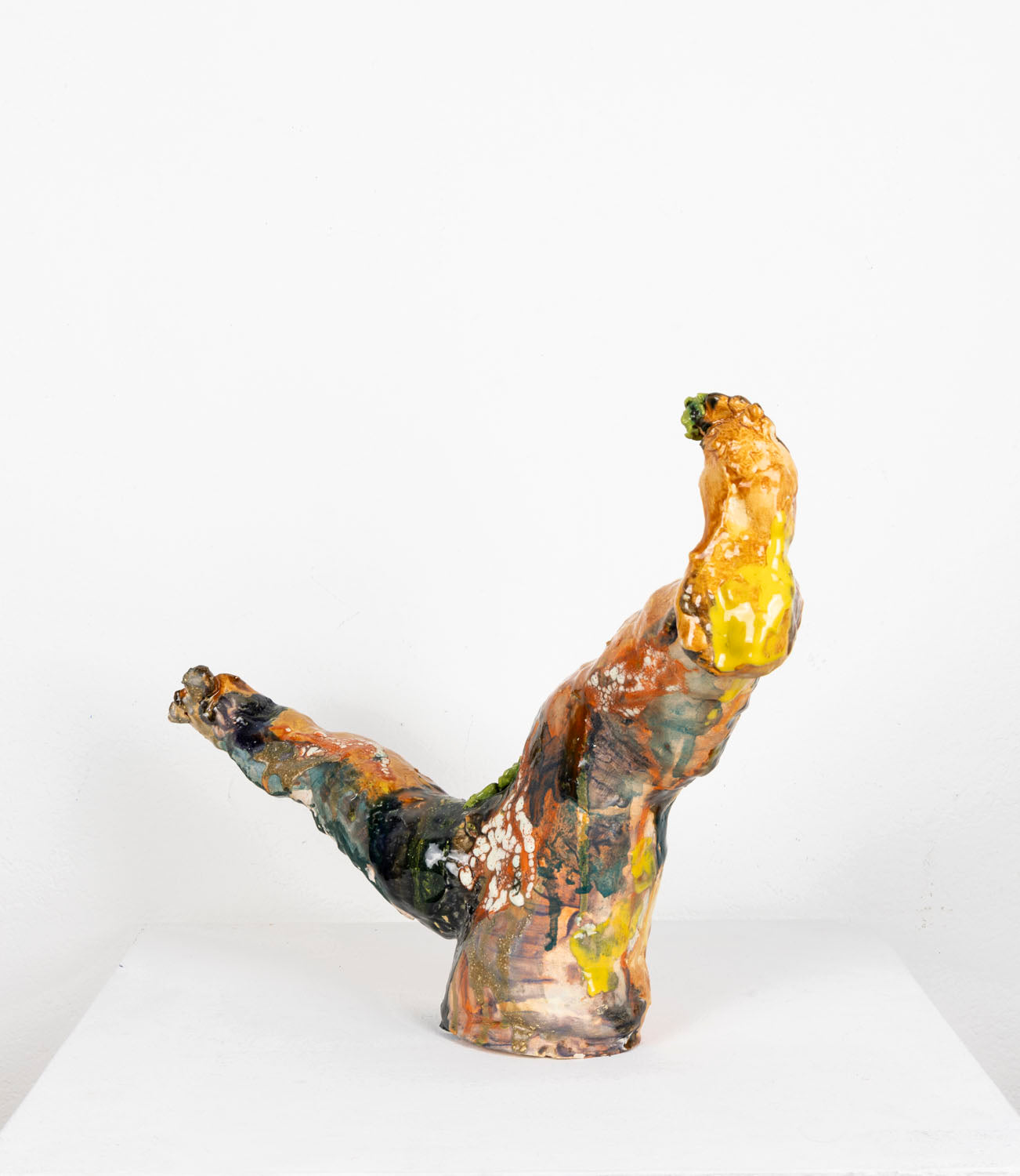 This is an abstract ceramic sculpture that resembles two upward-extending legs. The glossy surface features layered glazes, underglazes and Egyptian paste in earthy tones—rust orange, deep green, black, cream, and hints of yellow—with textured patches and drips.