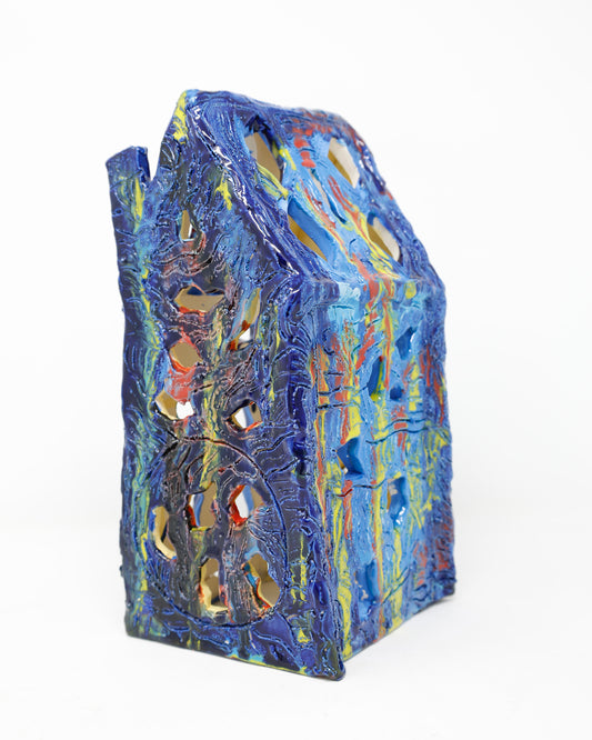 A ceramic house sculpture that has engravings and organic windows. The glaze is vibrant and runny, with a combination of blues, reds and yellows. 