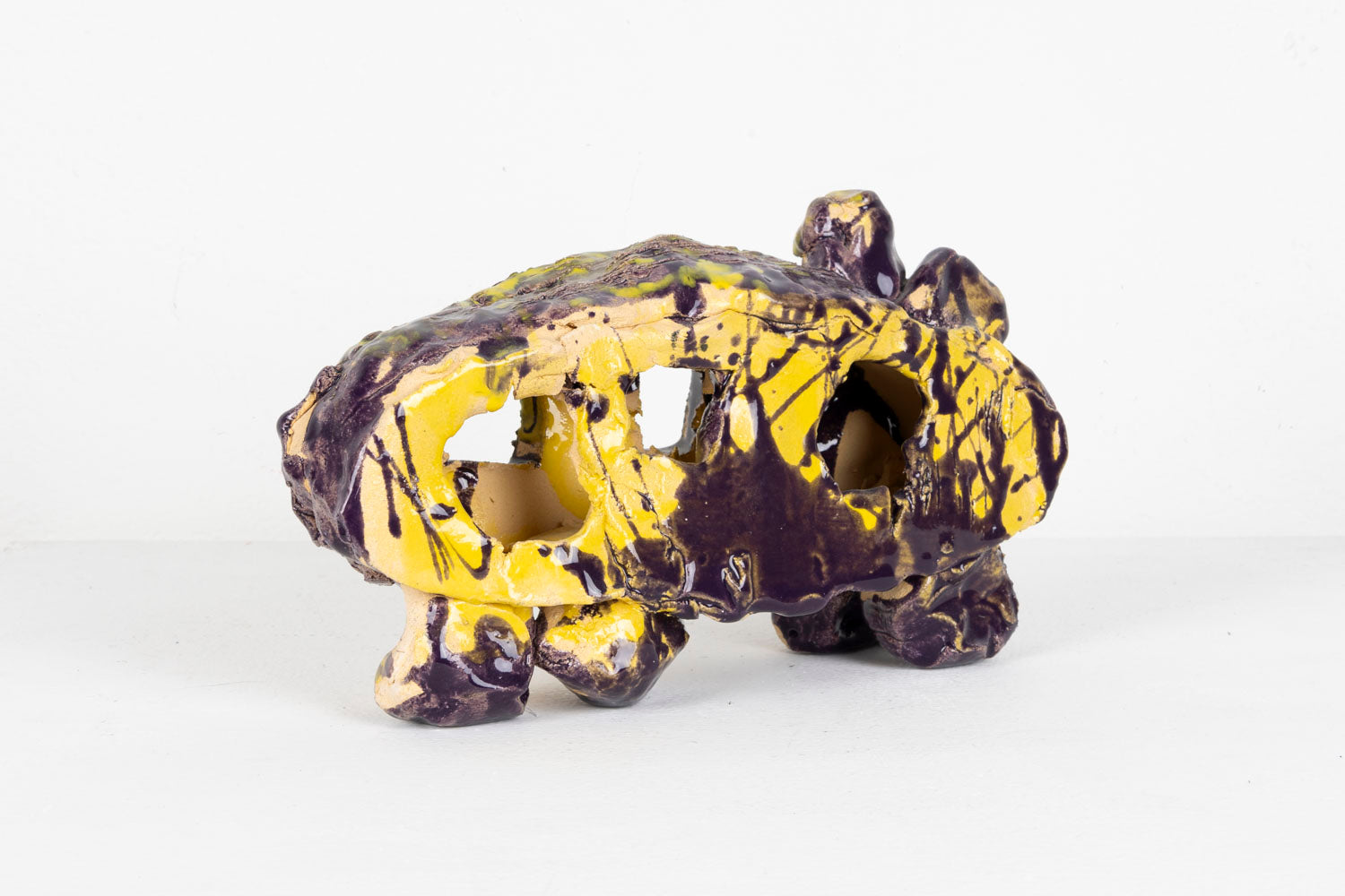 This is an abstracted ceramic sculpture of a car. The car is glazed with shades of purple and yellow.