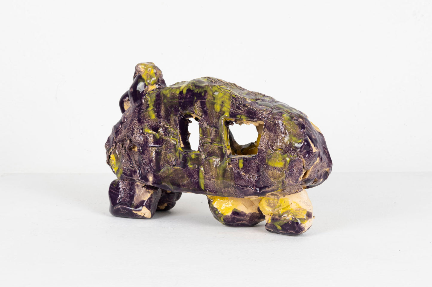 This is an abstracted ceramic sculpture of a car. The car is glazed with shades of black, purple and yellow.