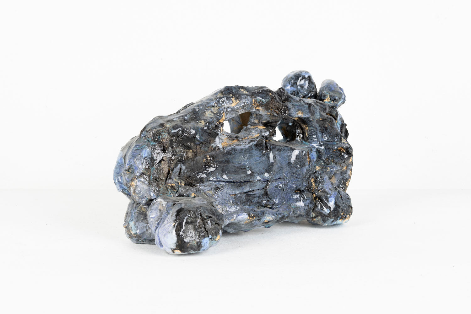This is an abstracted ceramic sculpture of a car. The car is glazed with shades of black, blue and purple. 