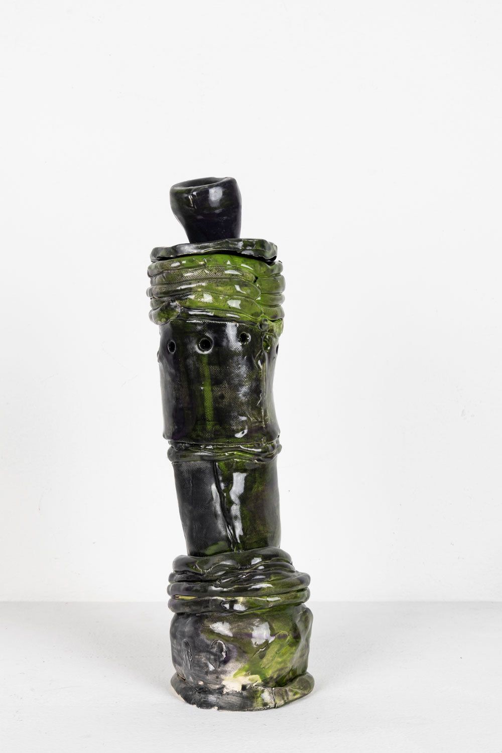 This is a ceramic sculpture contains three elements that come together to form a depiction of a hookah. The piece is predominantly a black glaze, with green highlights.