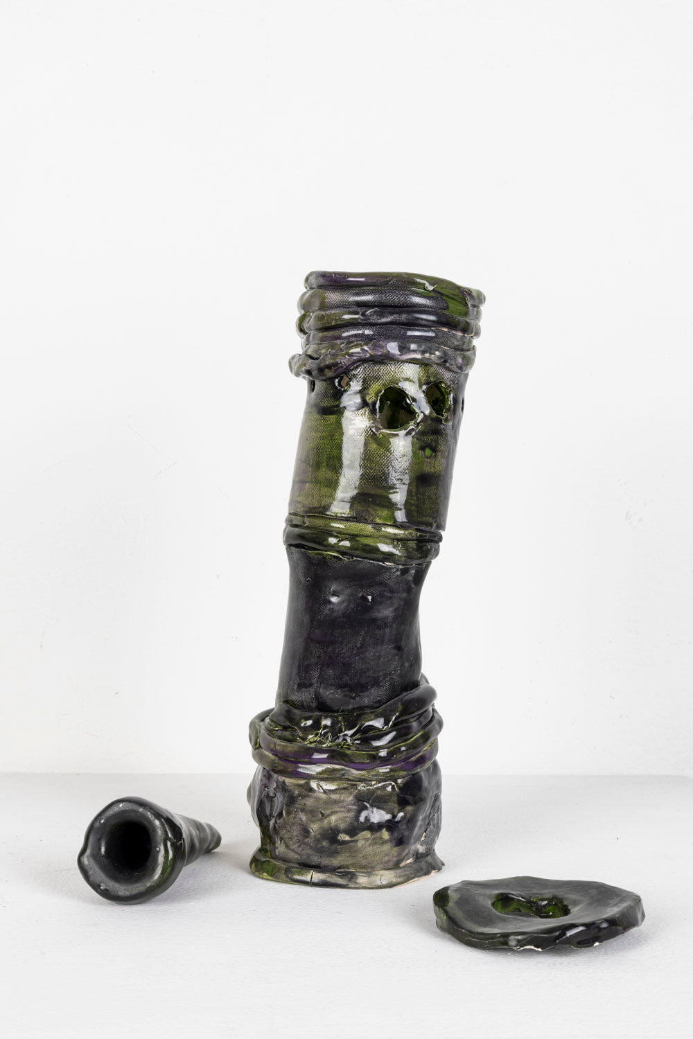 This is a ceramic sculpture contains three elements that come together to form a depiction of a hookah. The piece is predominantly a black glaze, with green highlights.