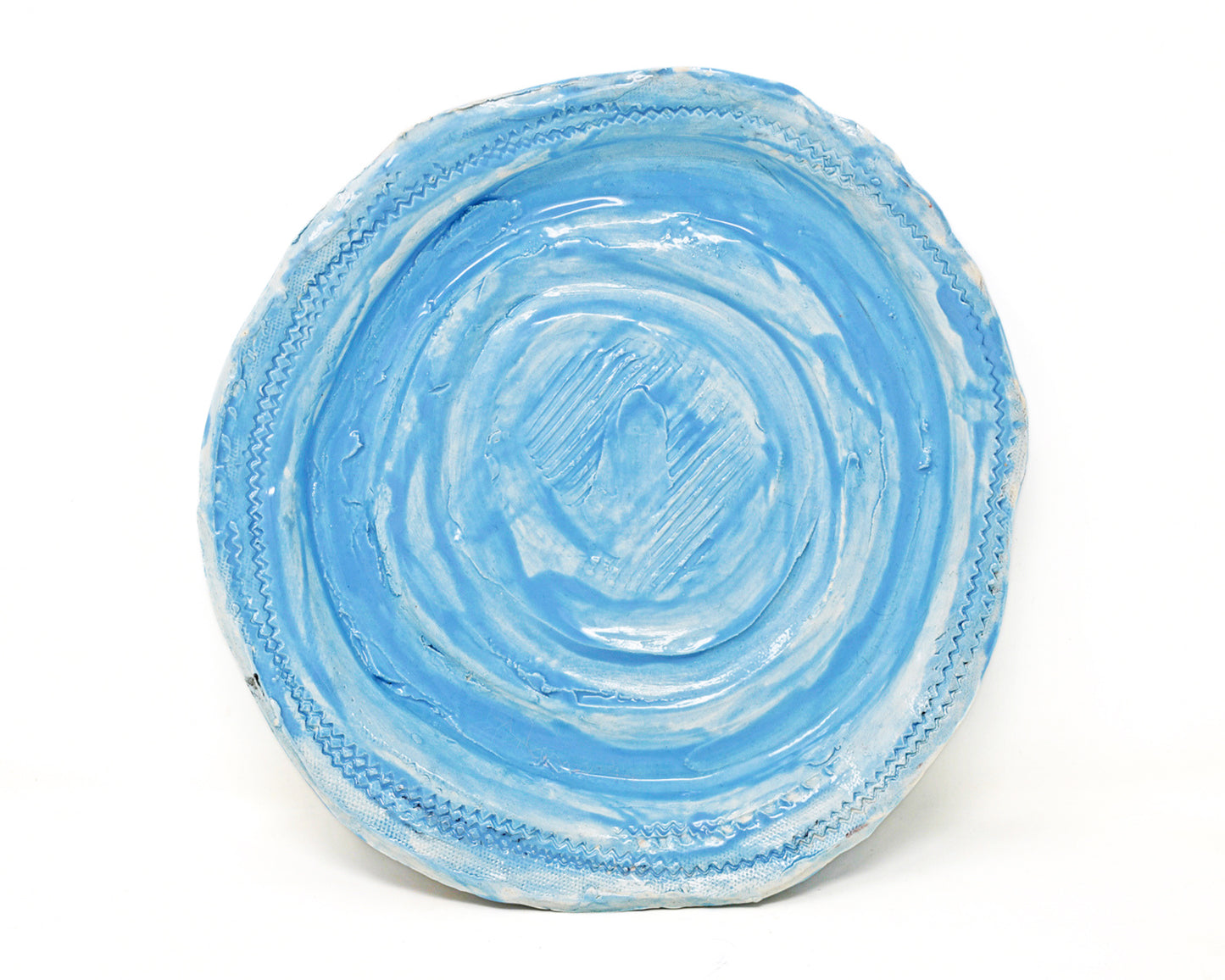 This ceramic plate is glazed light blue. There are carved details along the edges of the plate, and in the center. 