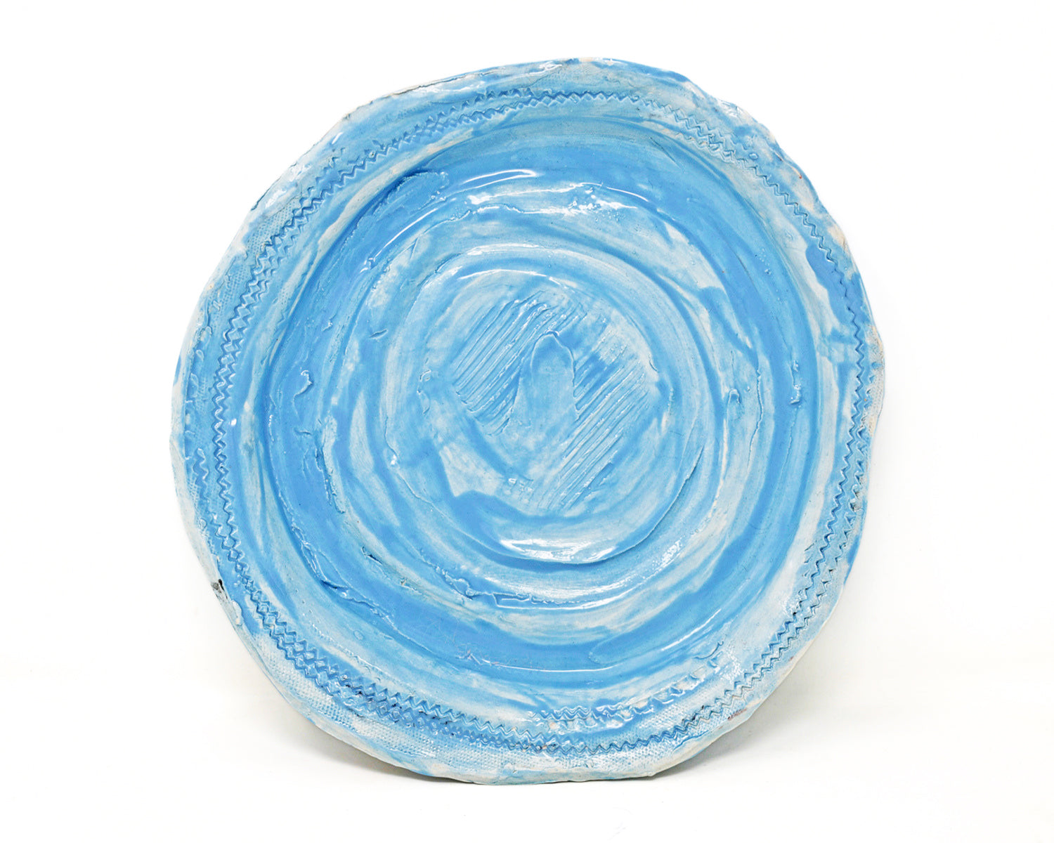 This ceramic plate is glazed light blue. There are carved details along the edges of the plate, and in the center. 