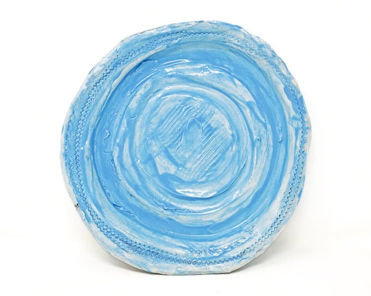 This ceramic plate is glazed light blue. There are carved details along the edges of the plate, and in the center. 