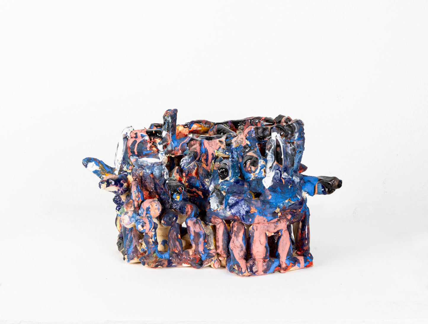 a ceramic sculpture of a two-tiered, cage-like structure glazed in shiny blue and matte pink. The structure is made of little cylinders, some are stacked vertically, others are wrapped around the form in horizontal bands, and several radiate out around the perimeter. There are gaps between each cylinder through which the white background is visible.