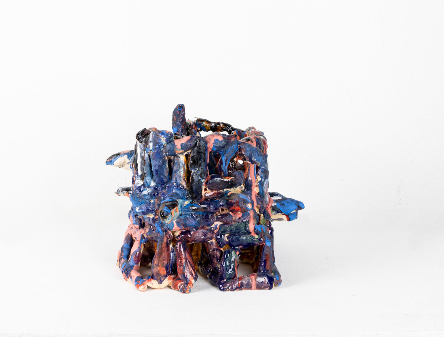 a ceramic sculpture of a two-tiered, cage-like structure glazed in shiny blue and matte pink. The structure is made of little cylinders, some are stacked vertically, others are wrapped around the form in horizontal bands, and several radiate out around the perimeter. There are gaps between each cylinder through which the white background is visible.
