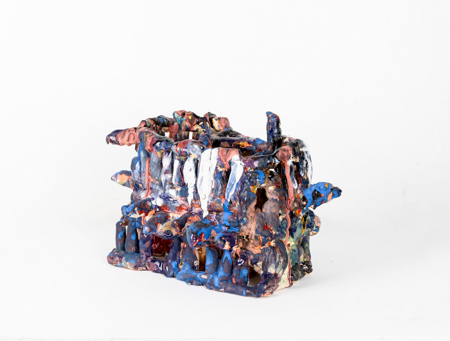 a ceramic sculpture of a two-tiered, cage-like structure glazed in shiny blue and matte pink. The structure is made of little cylinders, some are stacked vertically, others are wrapped around the form in horizontal bands, and several radiate out around the perimeter. There are gaps between each cylinder through which the white background is visible.