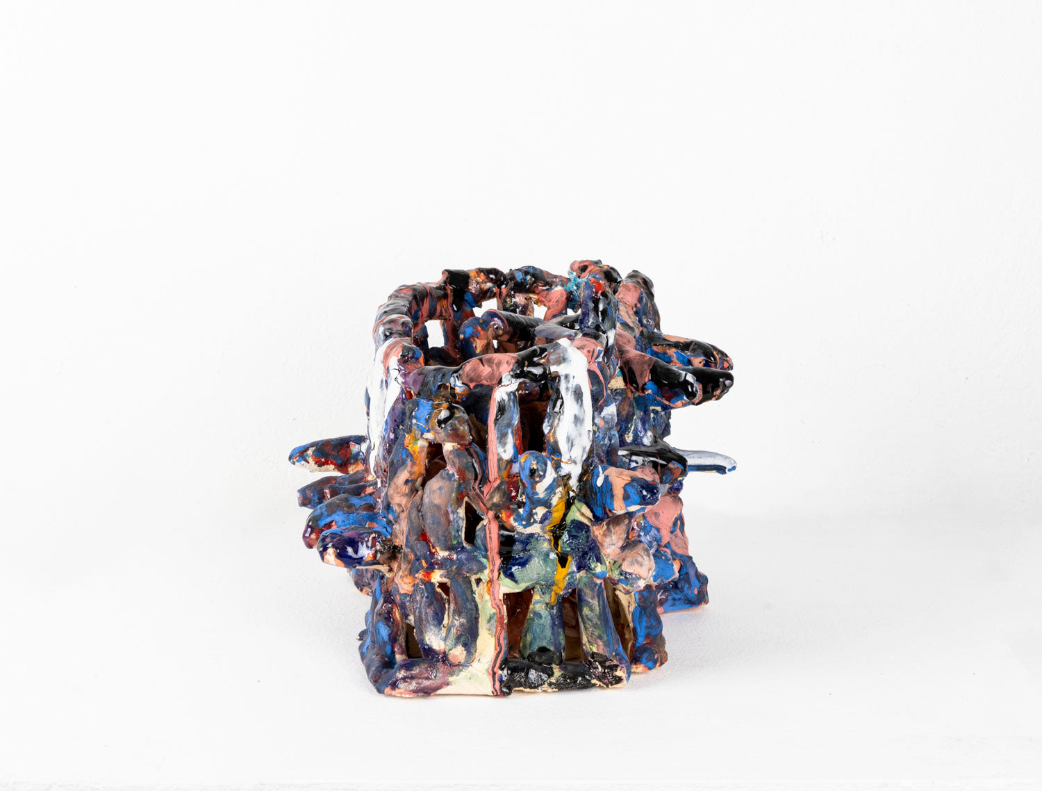 a ceramic sculpture of a two-tiered, cage-like structure glazed in shiny blue, white, and matte pink. The structure is made of little cylinders, some are stacked vertically, others are wrapped around the form in horizontal bands, and several radiate out around the perimeter. There are gaps between each cylinder through which the white background is visible.
