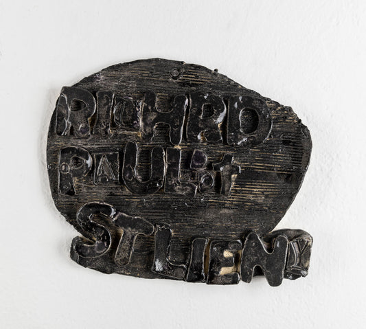 This is a ceramic sculpture that is contains the text 'Richrd Paul it Stlieny.' The text protrudes outwards from the piece, and is covered in a black glaze.