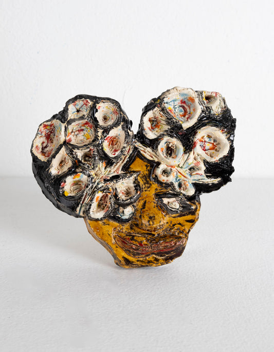 This is an abstracted ceramic sculpture of a figure, their facial features are depicted through black glaze for the eyes and a red glaze for the lips. The hair is in two buns, with white, blue and red patterns carved into the hair to create a floral look.