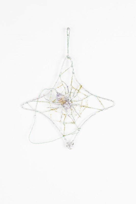 This mixed media sculpture is of a spider and its web. It is gold and silver, with hints of purple. There is a luminescent quality to the work, with the spider and the web blending into each other. 