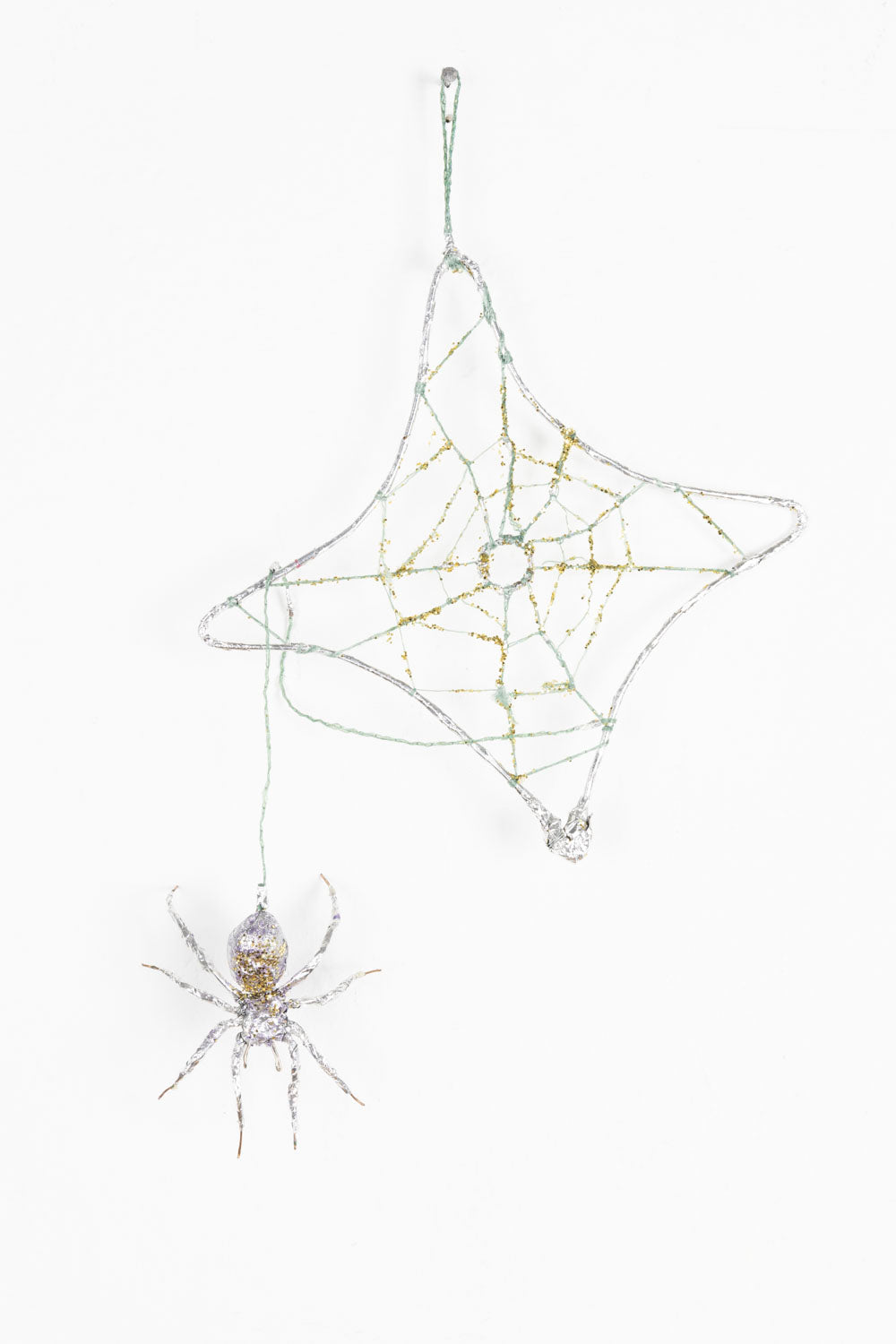 This mixed media sculpture is of a spider and its web. It is gold and silver, with hints of purple. There is a luminescent quality to the work, with the spider and the web blending into each other. 