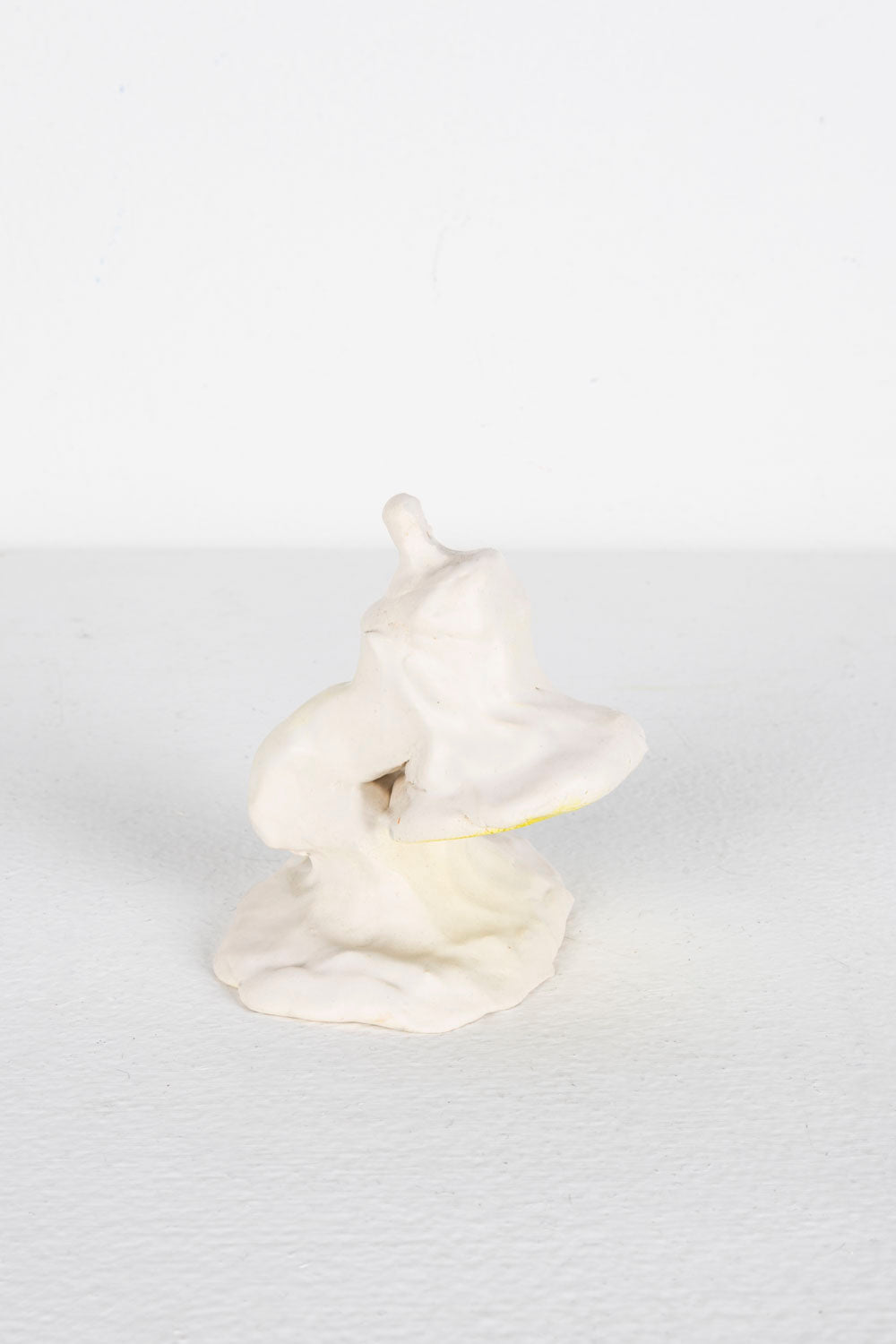 This is a ceramic piece depicting a Mini Luxo. It is glazed predominantly in white, with yellow highlights. 