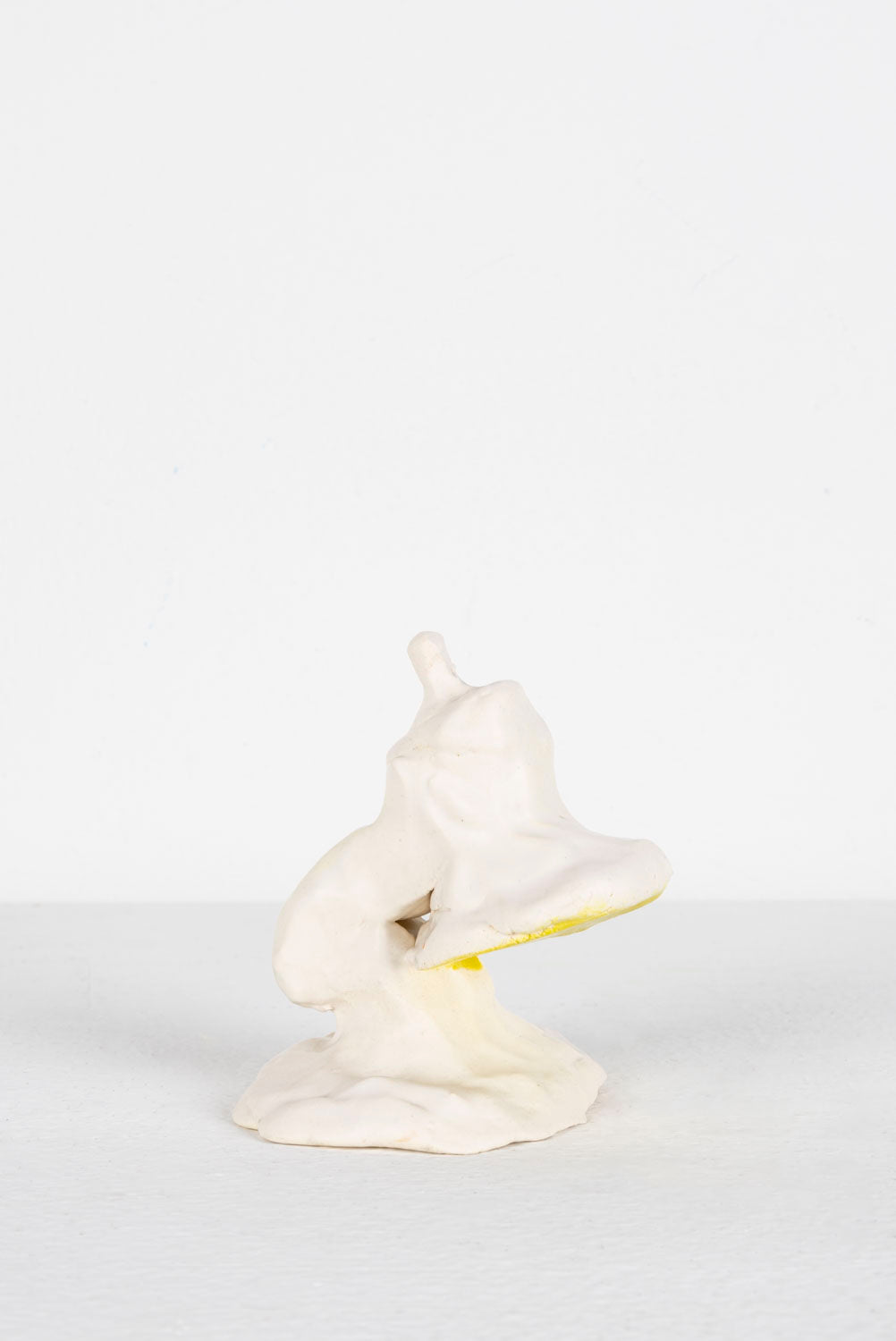 This is a ceramic piece depicting a Mini Luxo. It is glazed predominantly in white, with yellow highlights. 