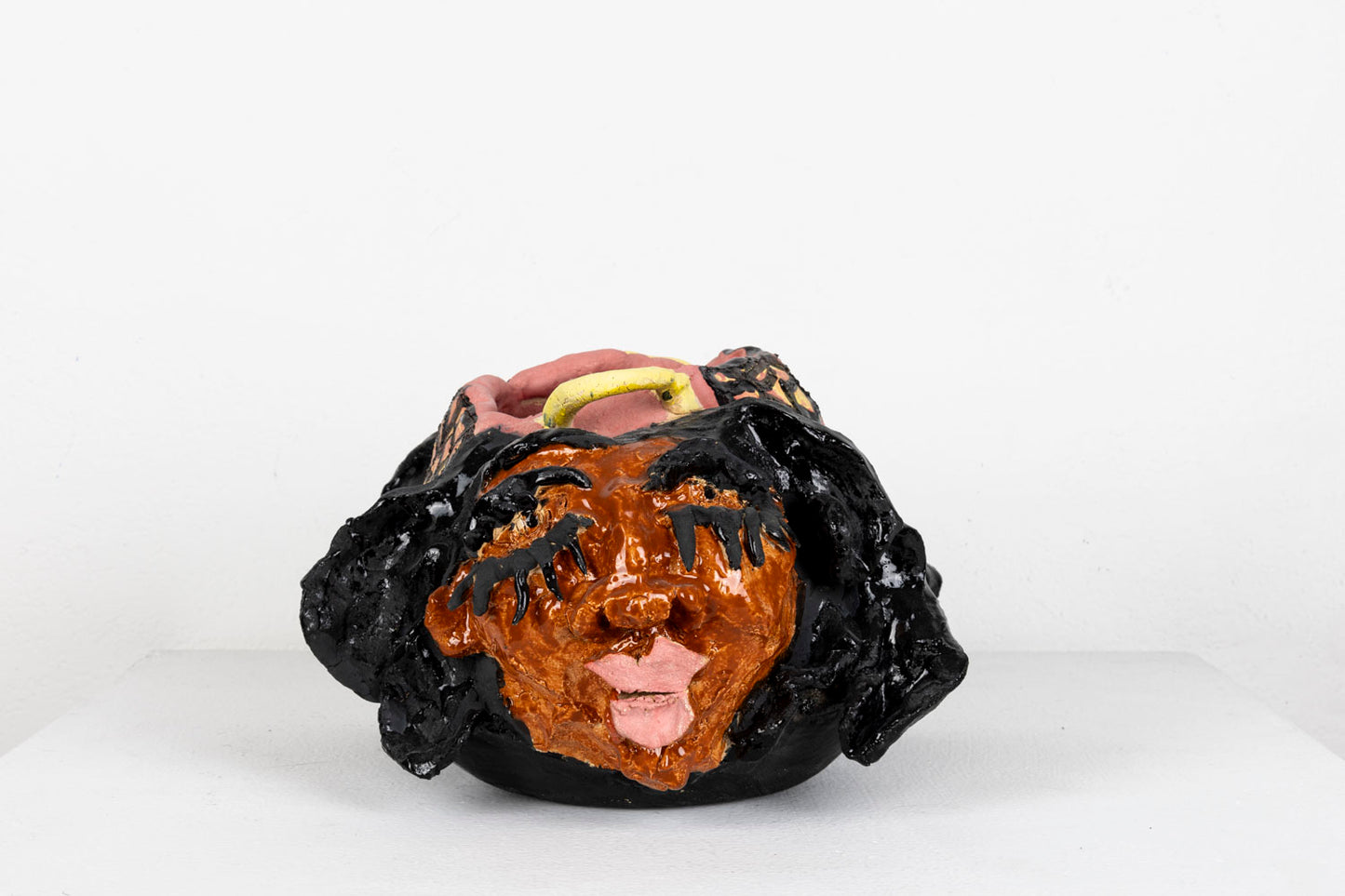 This sculpture is an abstracted figure, their facial features carved out, with pink glaze for the lips and black glaze for the eyelashes and hair.