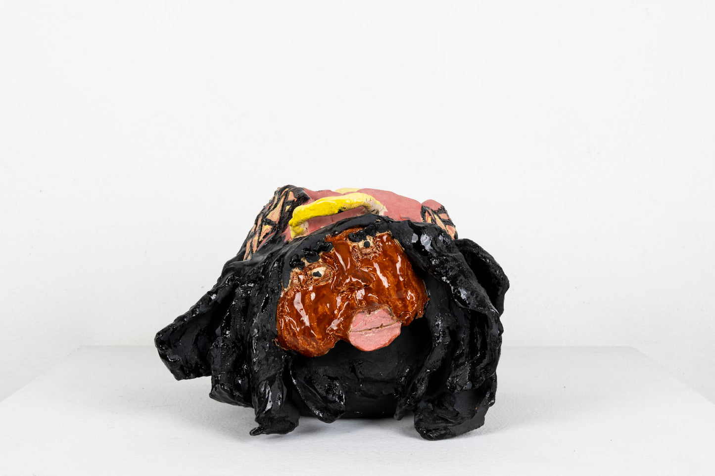 This sculpture is an abstracted figure, their facial features carved out, with pink glaze for the lips and black glaze for the eyelashes and hair.