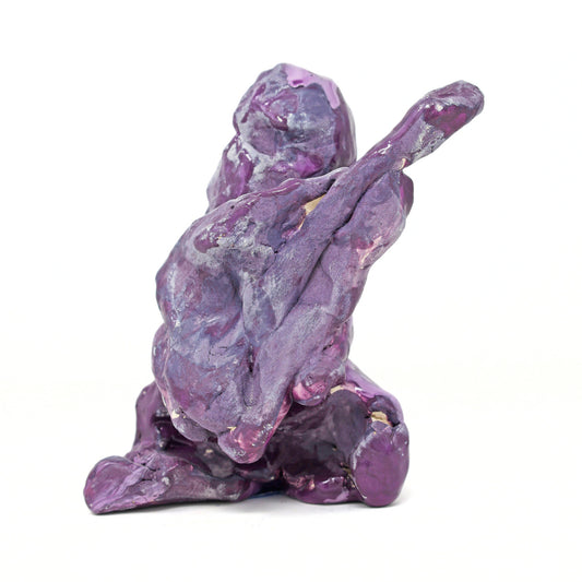 This is an abstracted ceramic sculpture of prince. There is a vague figurative form that is holding a guitar. The entire sculpture is glazed in shades of purple and blue. 
