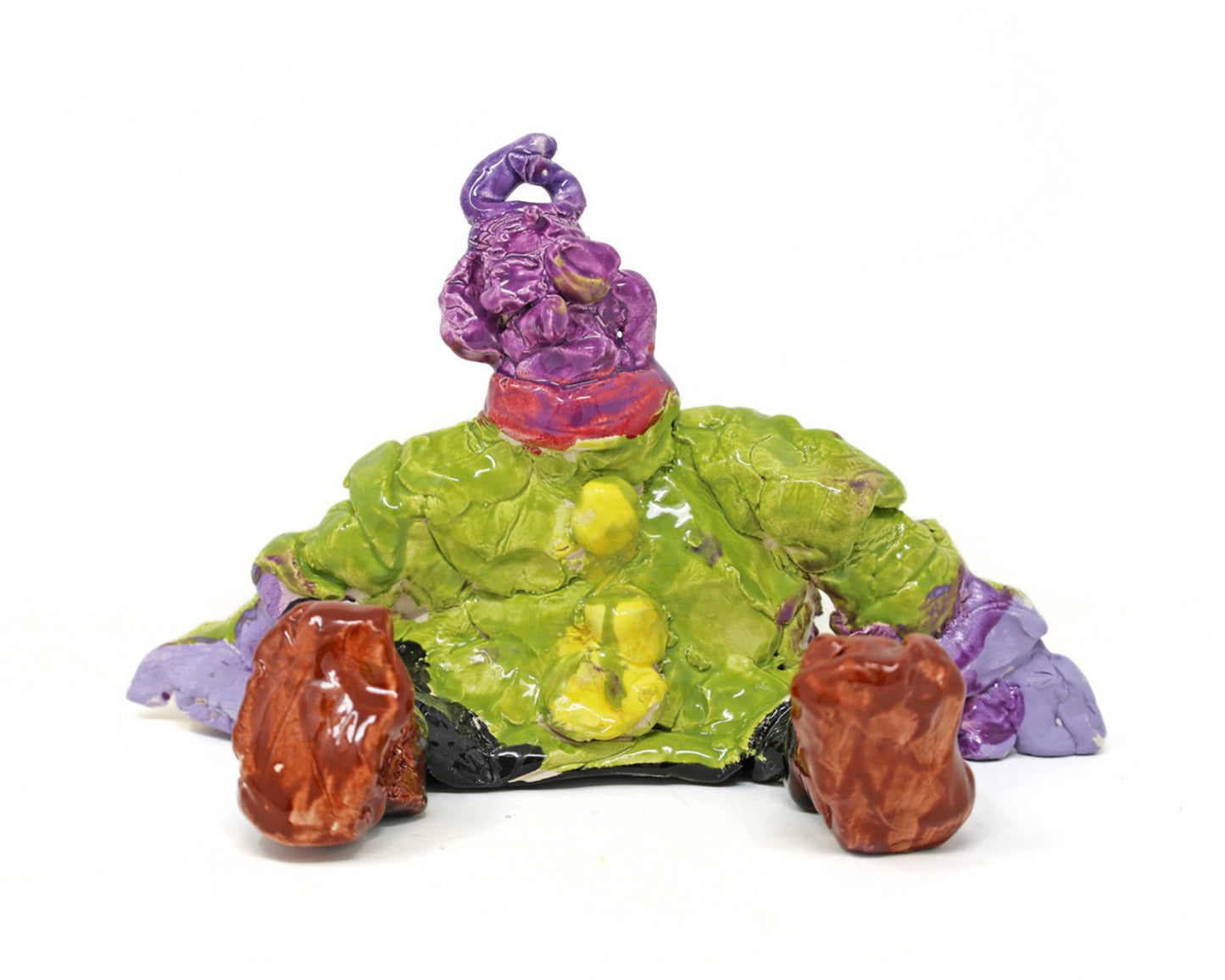This ceramic sculpture depicts a figure that is sitting down. The figure has purple skin, and is wearing a green shirt with yellow buttons, a red scarf, black pants and brown shoes. 