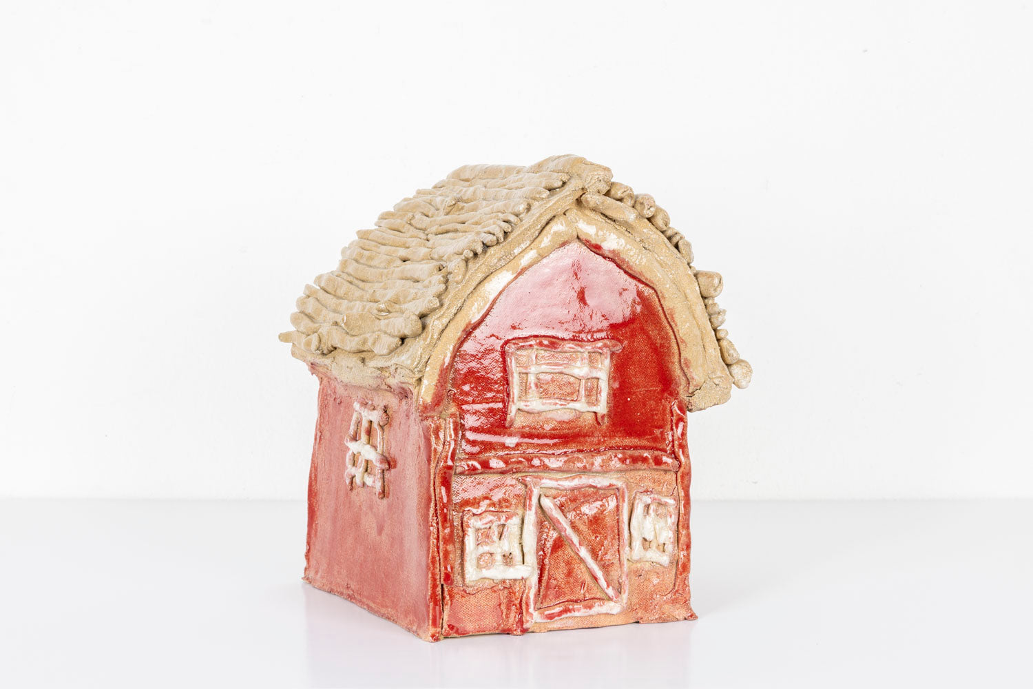 This is a ceramic sculpture of a house, glazed with vibrant hues of red and beige. The details of the house such as the windows and the doors are carved into the clay. 