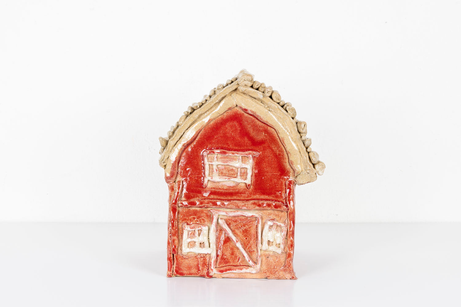 This is a ceramic sculpture of a house, glazed with vibrant hues of red and beige. The details of the house such as the windows and the doors are carved into the clay. 