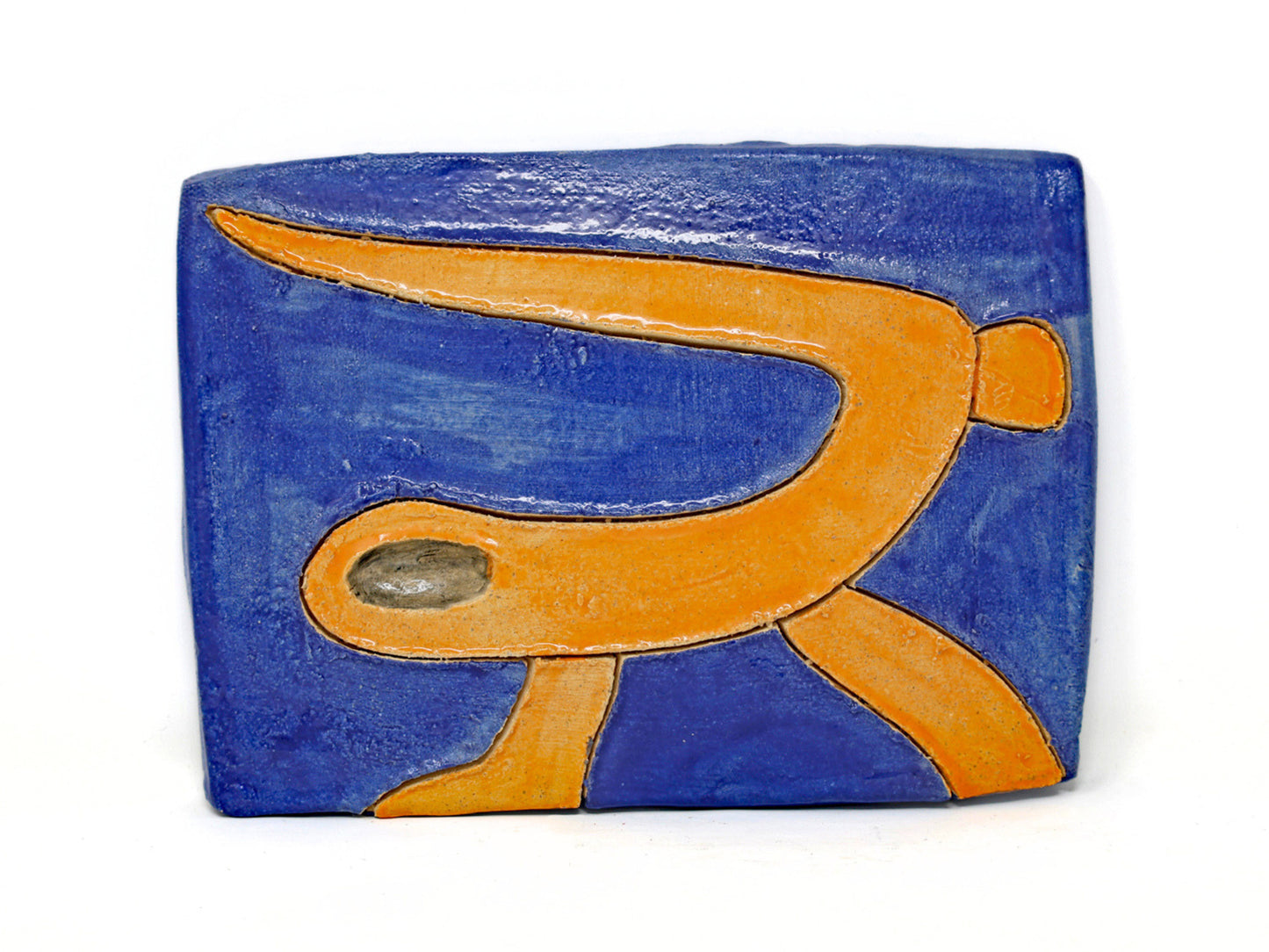This ceramic piece is a stylized depiction of a sea snake. The sea snake is glazed in a bright orange which complements the dark blue background. The sea snake is carved out from the piece. 
