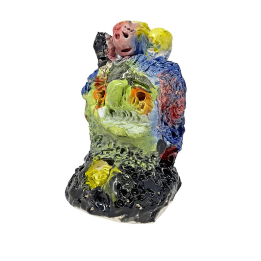 A chaotic ceramic sculpture - a mottled surface of lime greens, blues, pinks and yellows on a black base. A head with sunken orange eyes with smaller heads protruding from the top.