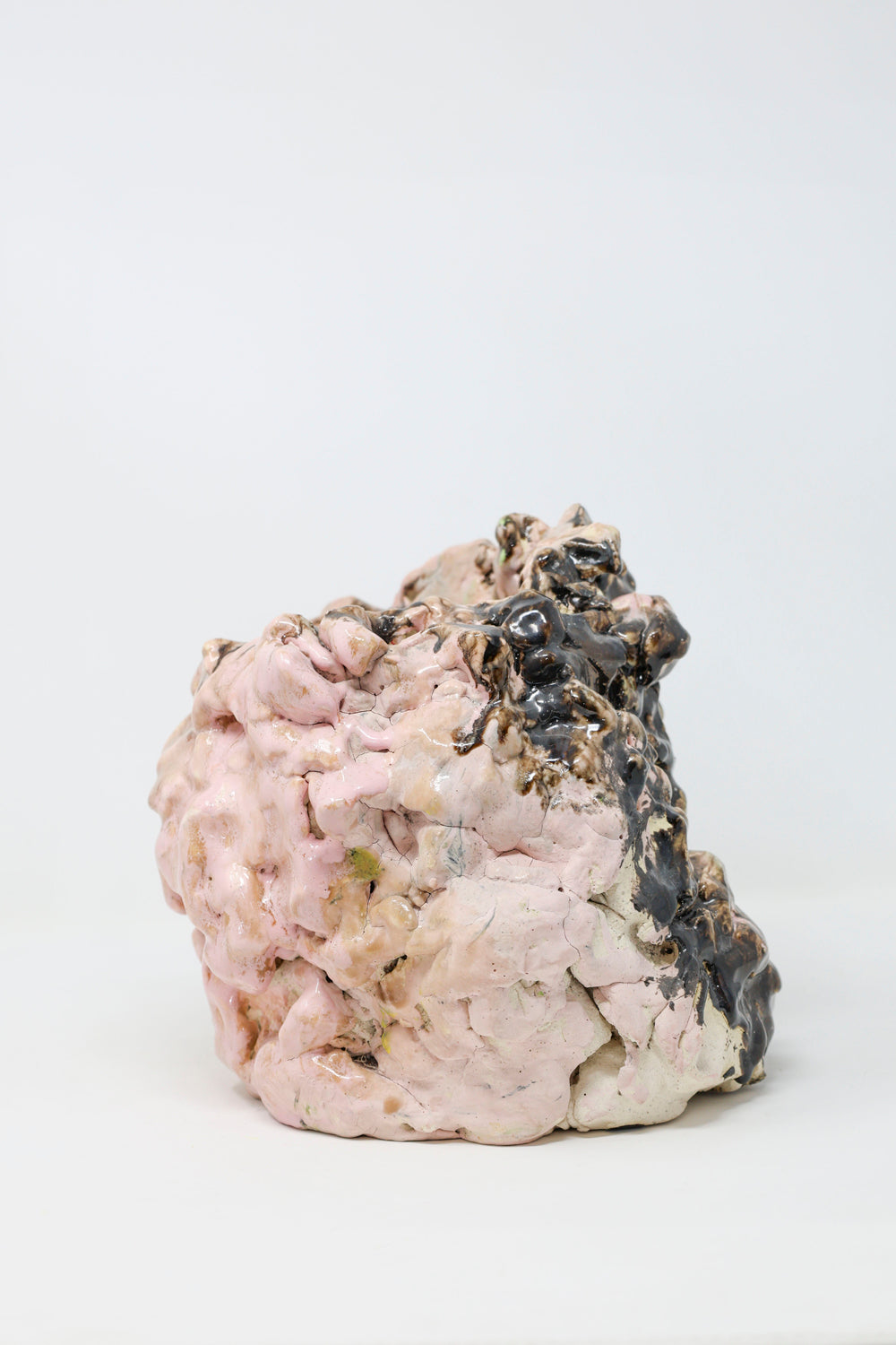 Abstract ceramic sculpture, lumpy in form and glossy in texture, colored with pink and black glaze. 