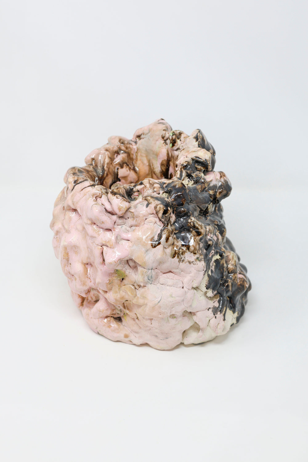 Abstract ceramic sculpture, lumpy in form and glossy in texture, colored with pink and black glaze. 