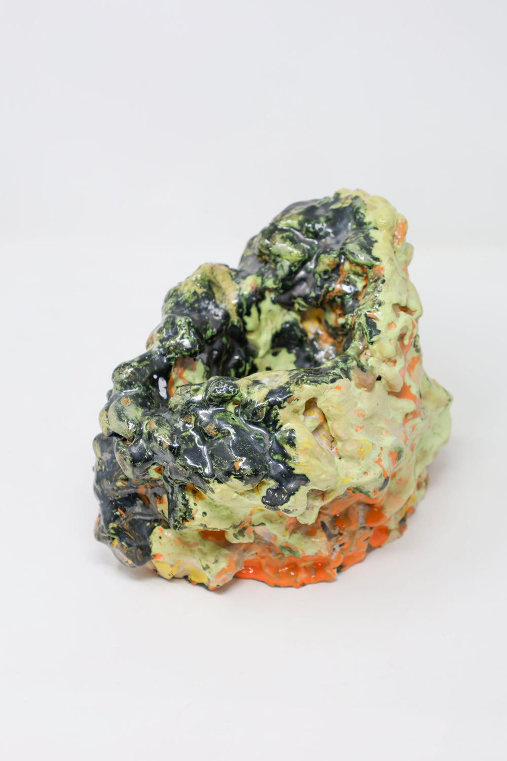 Abstract hollow ceramic sculpture, lumpy in form and glossy in texture, colored with green, orange and black glaze. 
