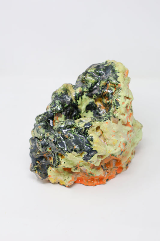 Abstract hollow ceramic sculpture, lumpy in form and glossy in texture, colored with green, orange and black glaze. 