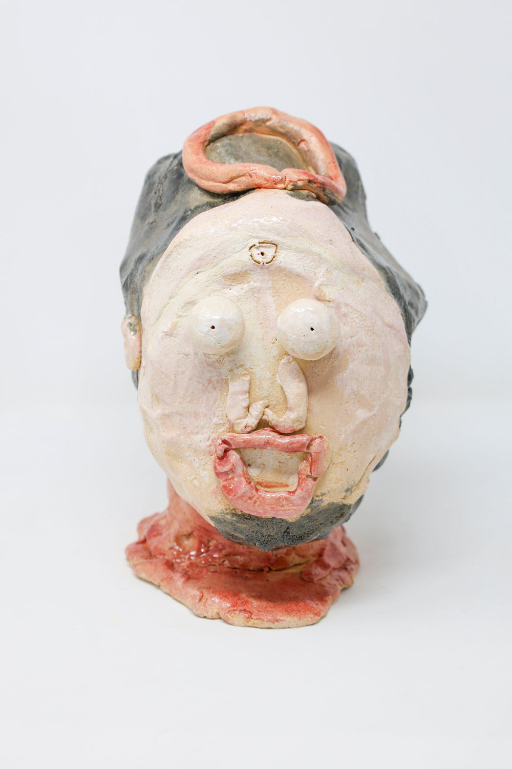 Ceramic sculpture of a head with features expressing fright. The figure has black hair and a goatee, a red neck and is wearing circular red crown. 