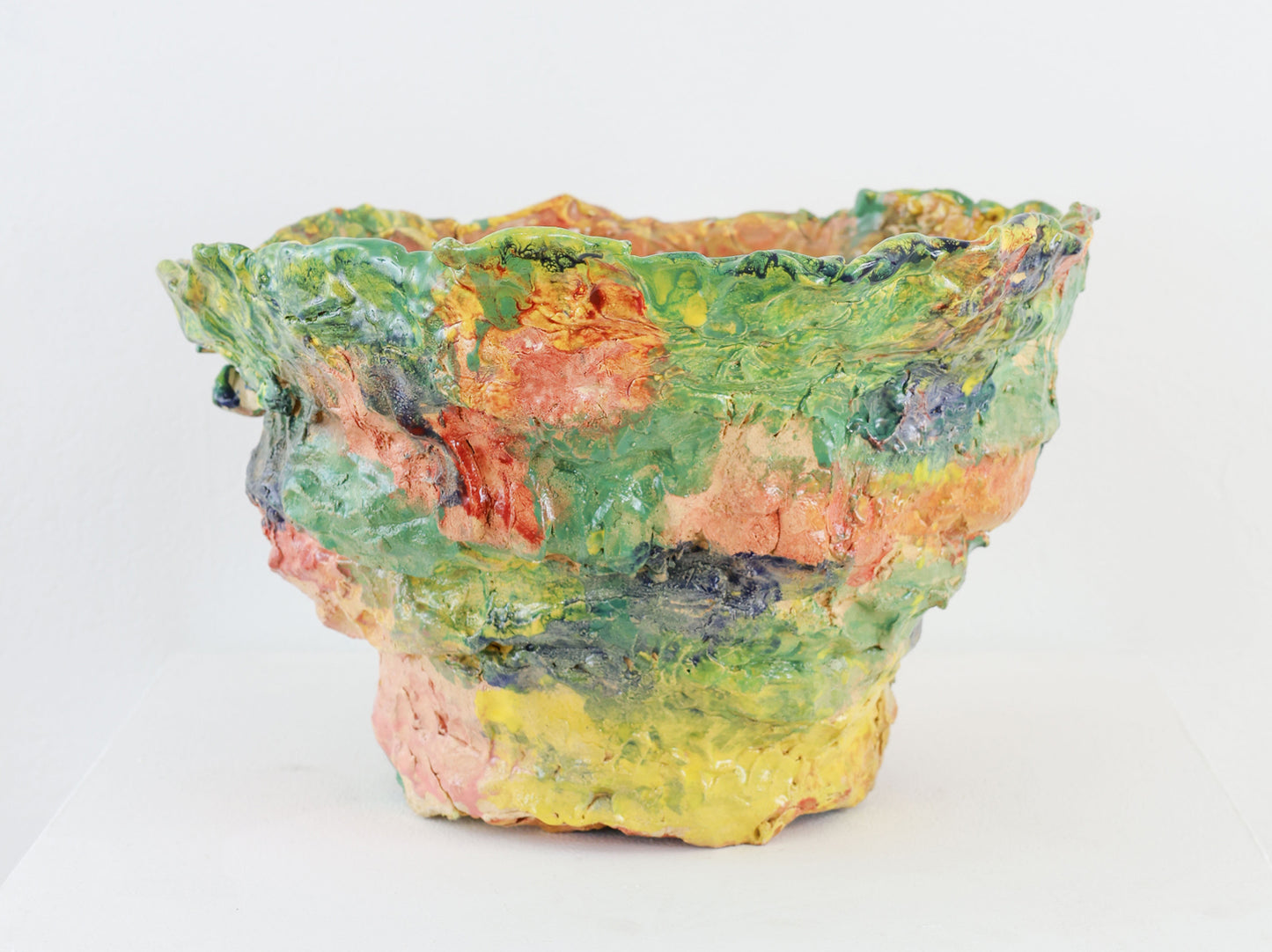 A highly textured colorful ceramic bowl with a rippled edge against a white background.