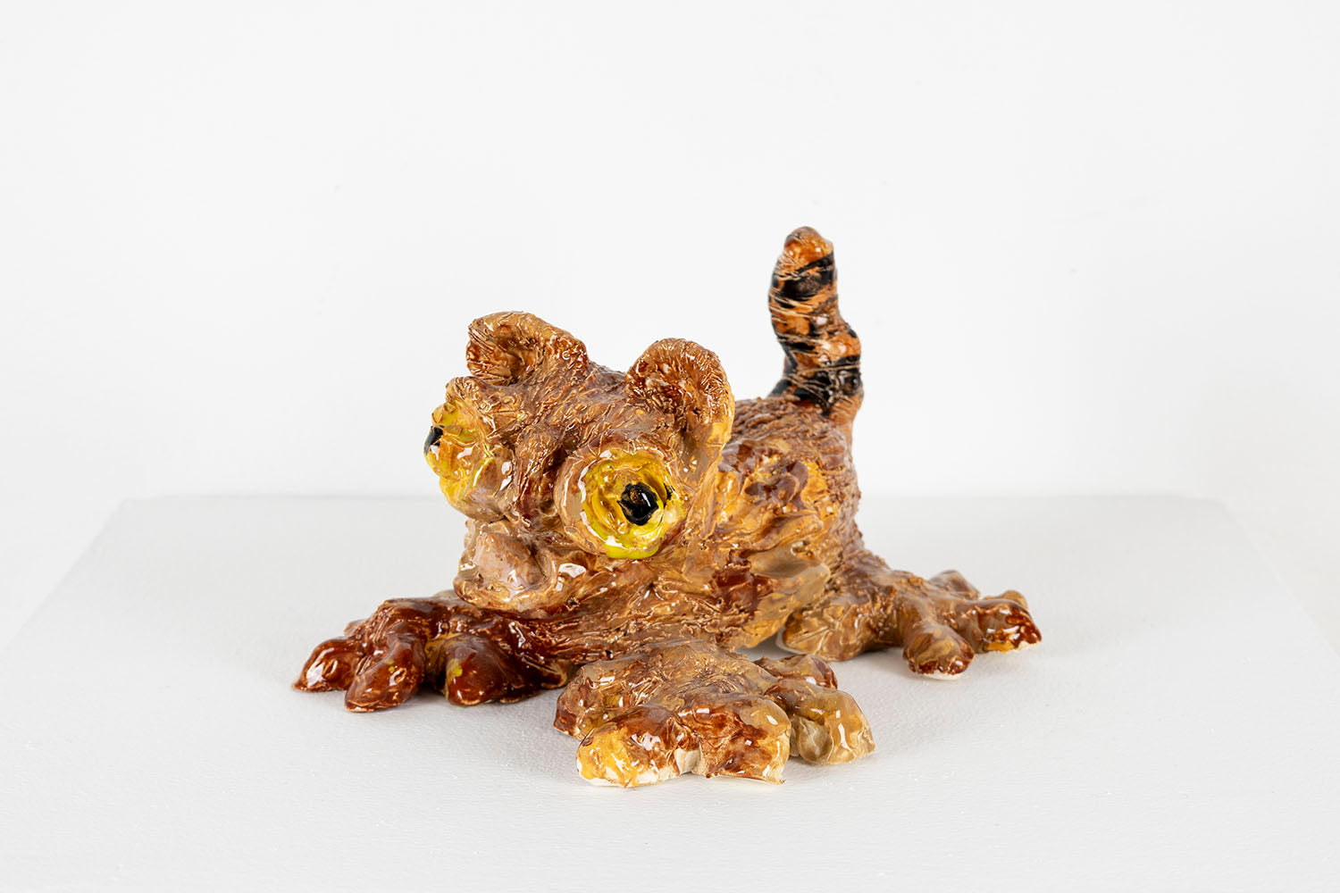 The same ceramic kitten sculpture photographed from the side. From this angle, the black stripes on its tail are more clearly in view. 