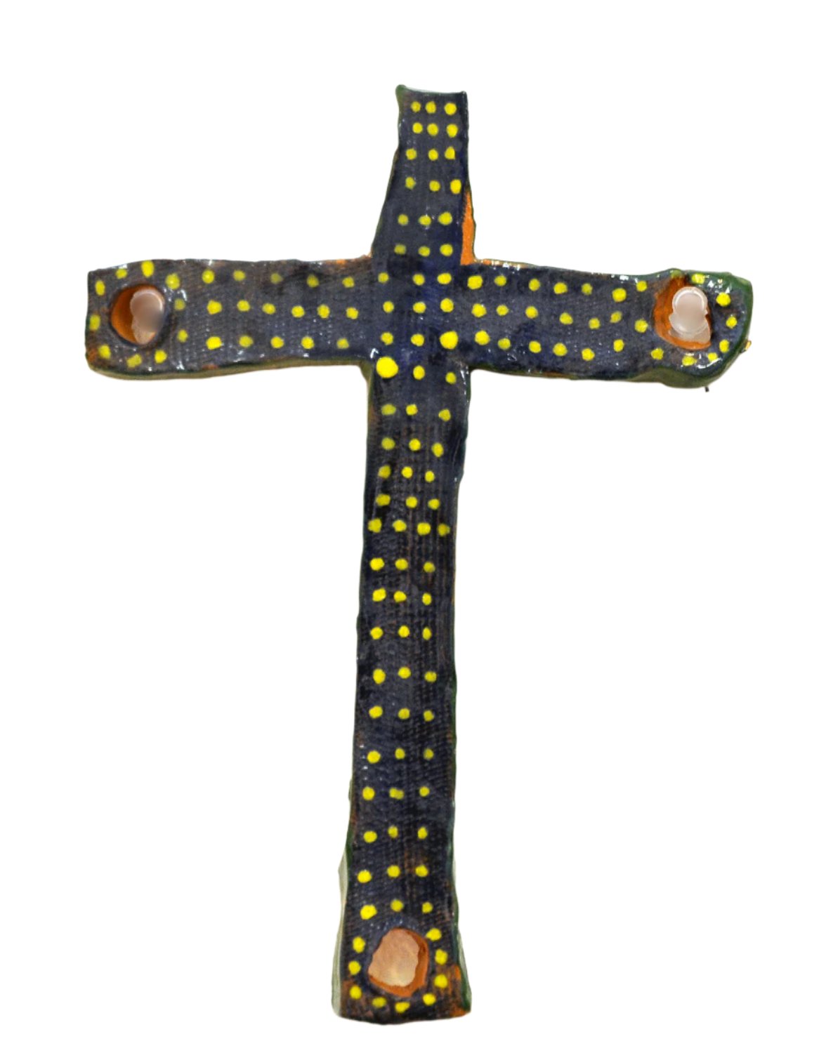 A handmade ceramic cross with a glossy dark blue-black surface covered in small yellow polka dots. The cross has an uneven, organic shape with circular openings near the ends of three arms, and it is displayed against a plain light gray background. 