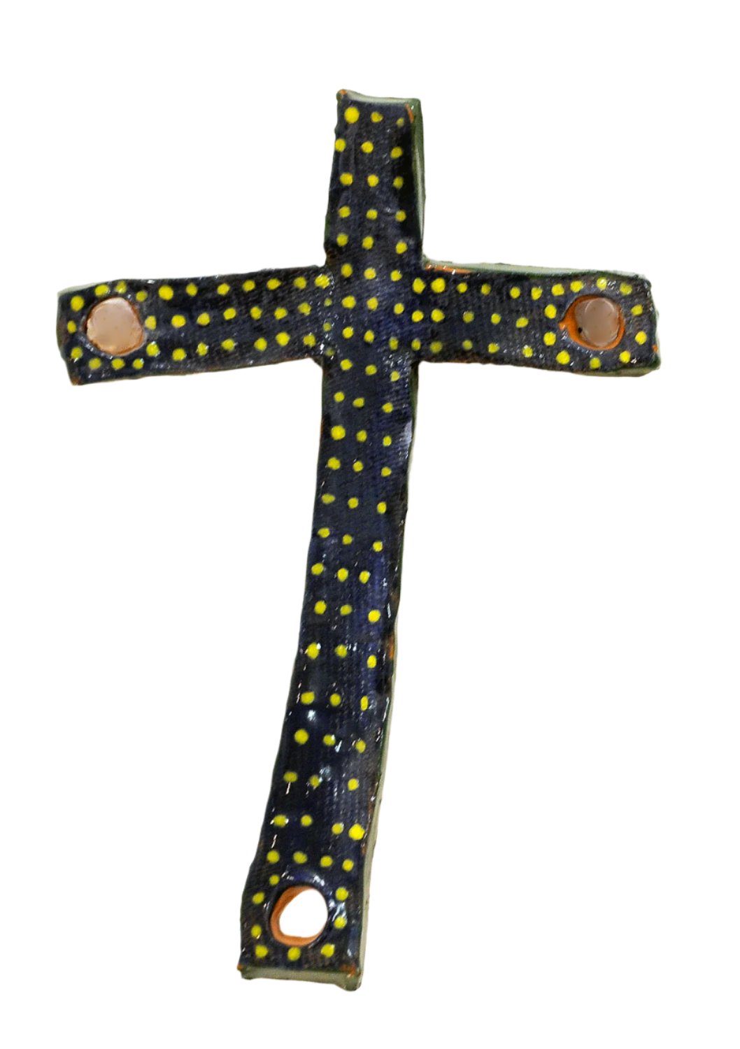 A handmade ceramic cross with a glossy dark blue-black surface covered in small yellow polka dots. The cross has an uneven, organic shape with circular openings near the ends of three arms, and it is displayed against a plain light gray background. 