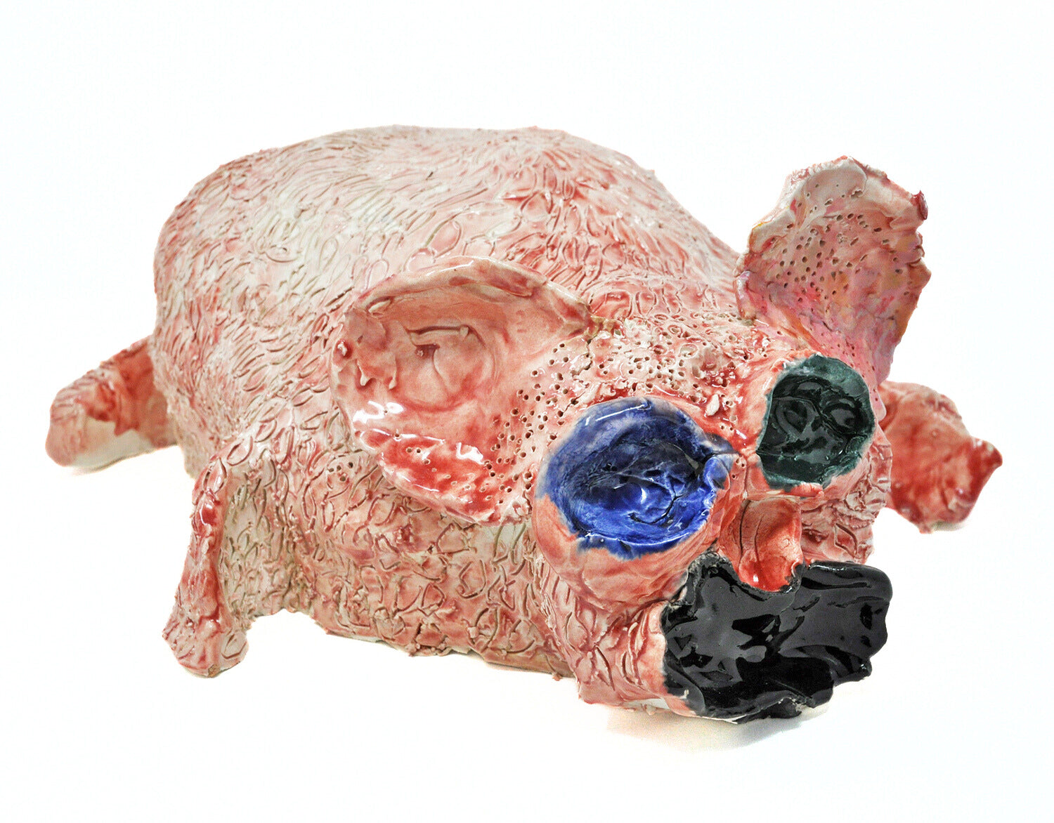 a ceramic sculpture of a small pink animal, similar to a rabbit or a piglet,  with round ears blue and black eyes, and a wide open black mouth. The surface of the sculpture is textured all over with etched dots and lines. 