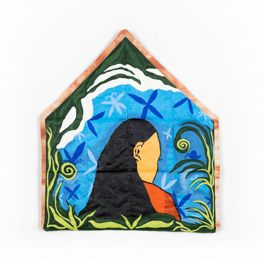 A medium tone skinned figure with long black hair faces turned away from the viewer with their side profile on display. Green plants frame a house shaped painted quilted canvas with blue skies and billowing white clouds. The edges of the paint quilt are dyed with pink madder root.