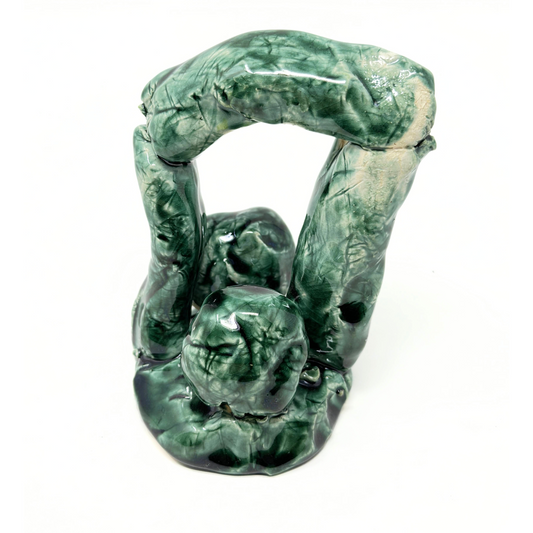 a small abstract ceramic sculpture. The structure features round ball shapes on a round base, with a tube arch assembled over them. The entire sculpture is glazed a glossy green color. 