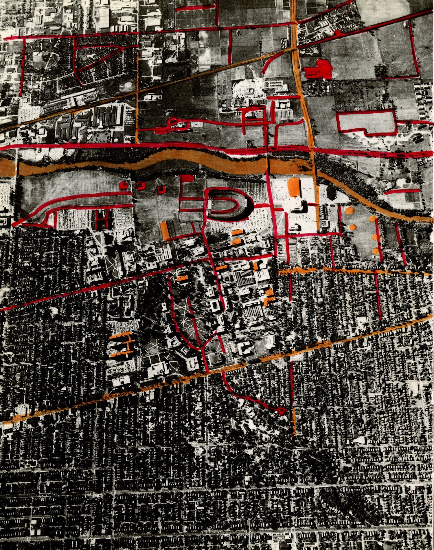 A black and white aerial photographic view of a city. Red and orange lines highlight different roads, buildings, and a river that runs horizontally across the top of the image. It looks like a map seen from above. The lines represent streets and alleys. The red markings stand out against the monochrome background, creating a strong contrast. The top two-thirds of the image includes colorful lines and larger, brighter surfaces, while the bottom part shows more dense and textured monochrome areas.