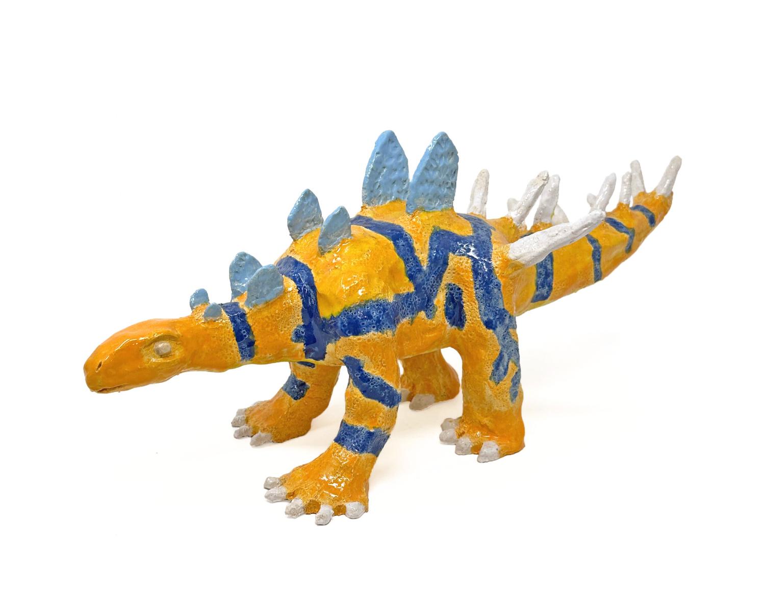 a small ceramic sculpture of a 4-legged dinosaur with a long tail. The dinosaur is glazed orange with a pattern of blue lines crisscrossing over its body. There is a row of flat blue spikes running the length of its back, and pointy white spikes lining its tail. 