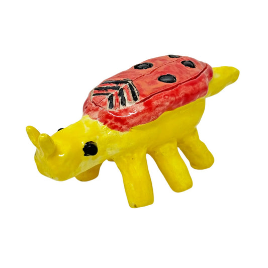 A small glazed ceramic figurine in the shape of a beetle. The form is a large round body balanced on 6 long tube legs. On the left, the insect has a cylindrical head with two short antennae sticking straight up, and two round black eyes. The sculpture is glazed all over in bright yellow, with red wings with black dots and stripes. 