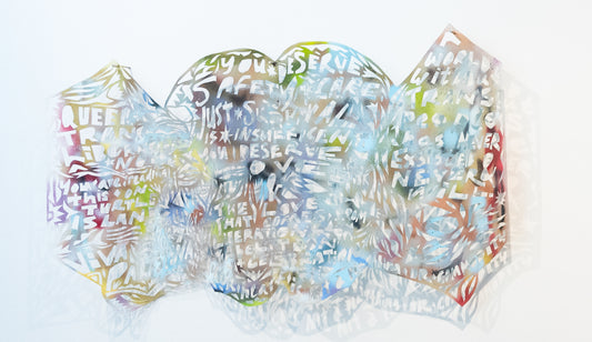 A kite-like bookform lays flat: its surface is covered in misty blue, pink, purple, green colors.Along with floral patterns of seedlets and starbursts, blocky hand cut text reads: 'Queer + Trans liberation now. You’re reading this on Turtle Island. ¡Viva Palestina! You deserve safety + care. Just survival is insufficient. You deserve love & the love that comes from liberation, abolition + celebration. Your heart is not a plaything or commodity. A world without Trans people has never existed & never will.'